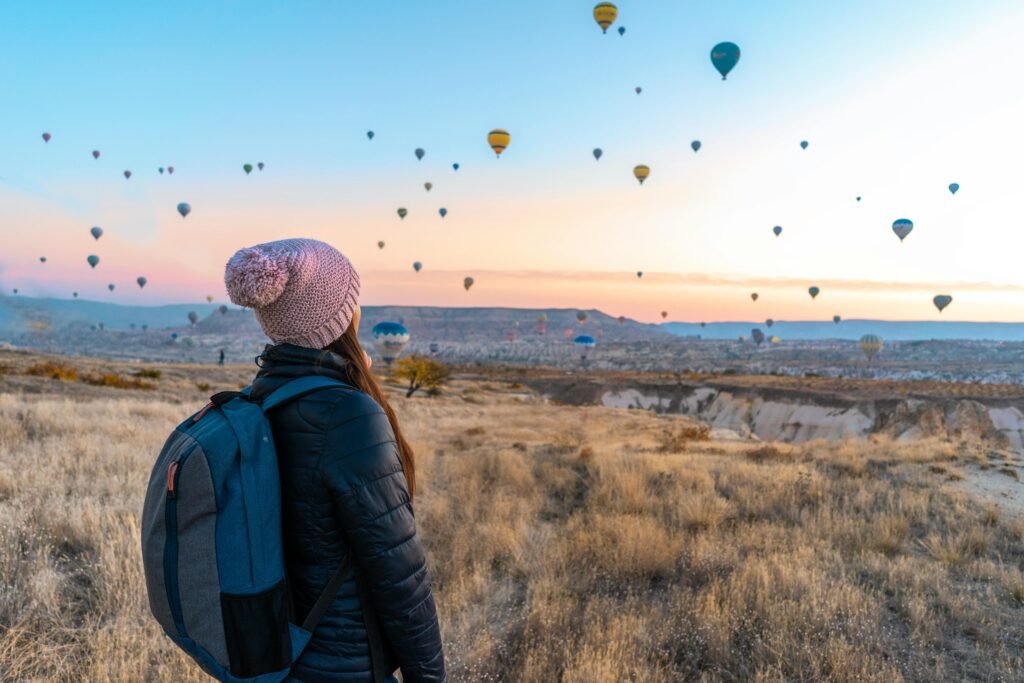 Woman in warm clothing staring at a lot of colourful hot-air balloons suspended in the air